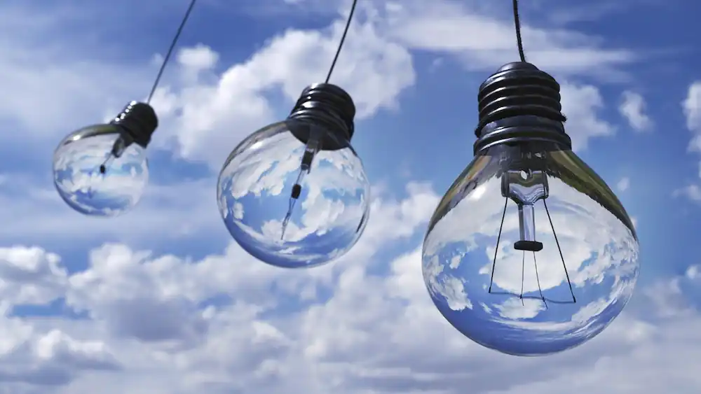 Three hanging light bulbs reflecting a blue sky with clouds in the background, symbolizing creativity and bright ideas.