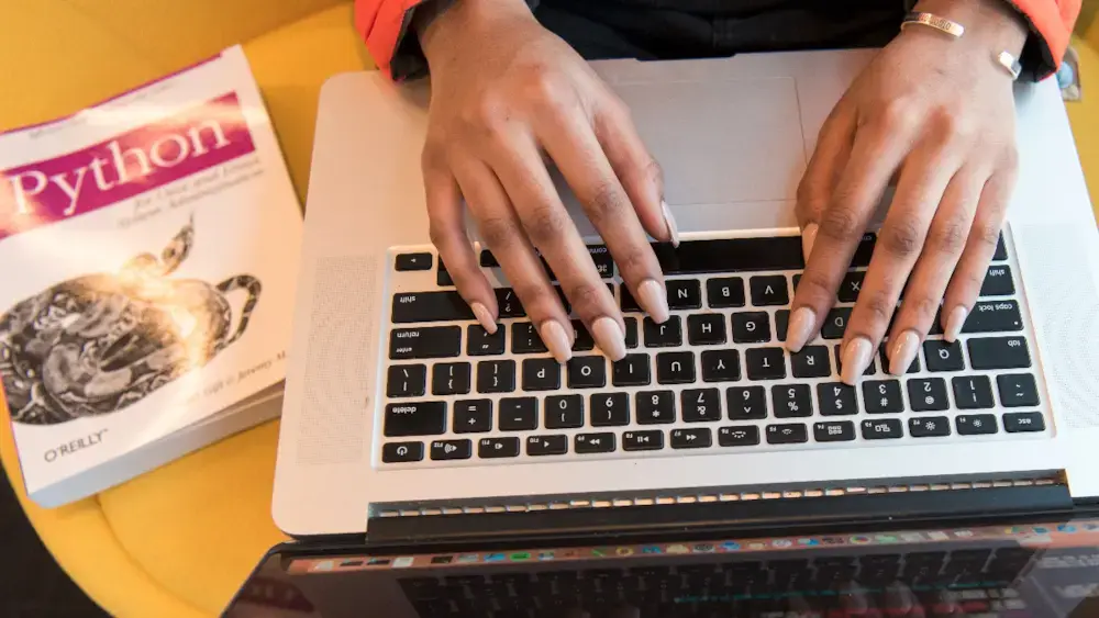 Typing in a laptop with a Python book on the side.