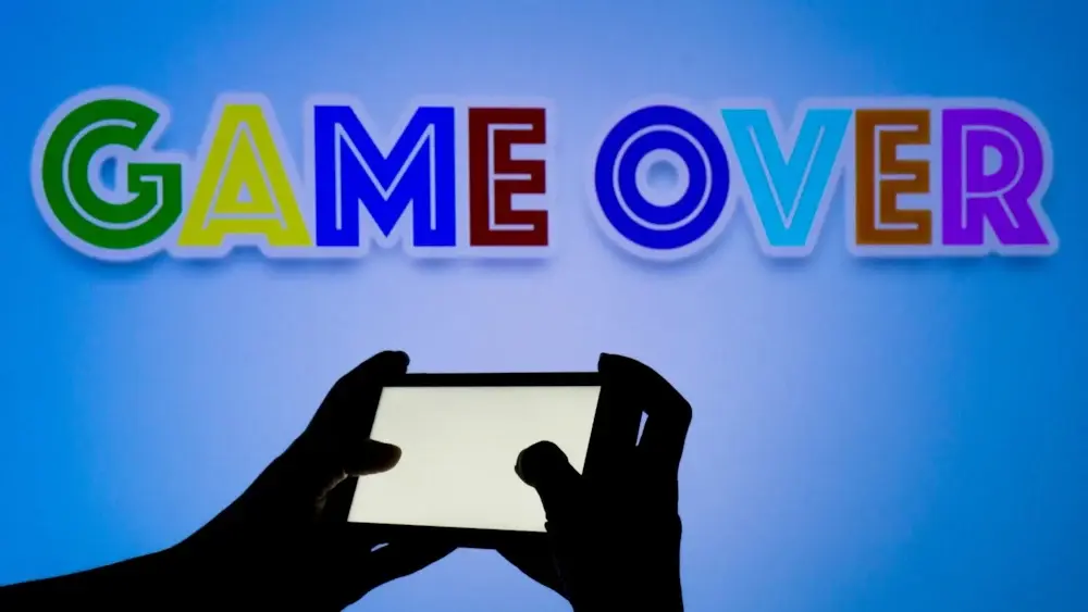 Mobile gaming concept; Close up of hands holding mobile phone; Colourful 'Game Over' text above
