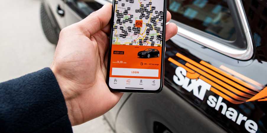 Close up of person using Sixt car share app with black Sixt car in background